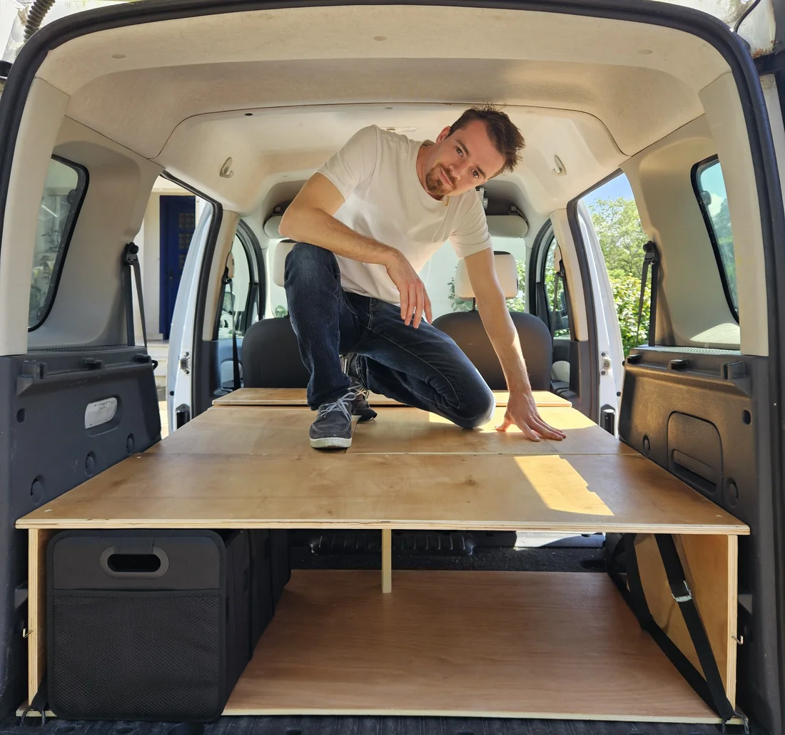 Henri, créateur du MiniVan Kit, assis dans son Kangoo aménagé